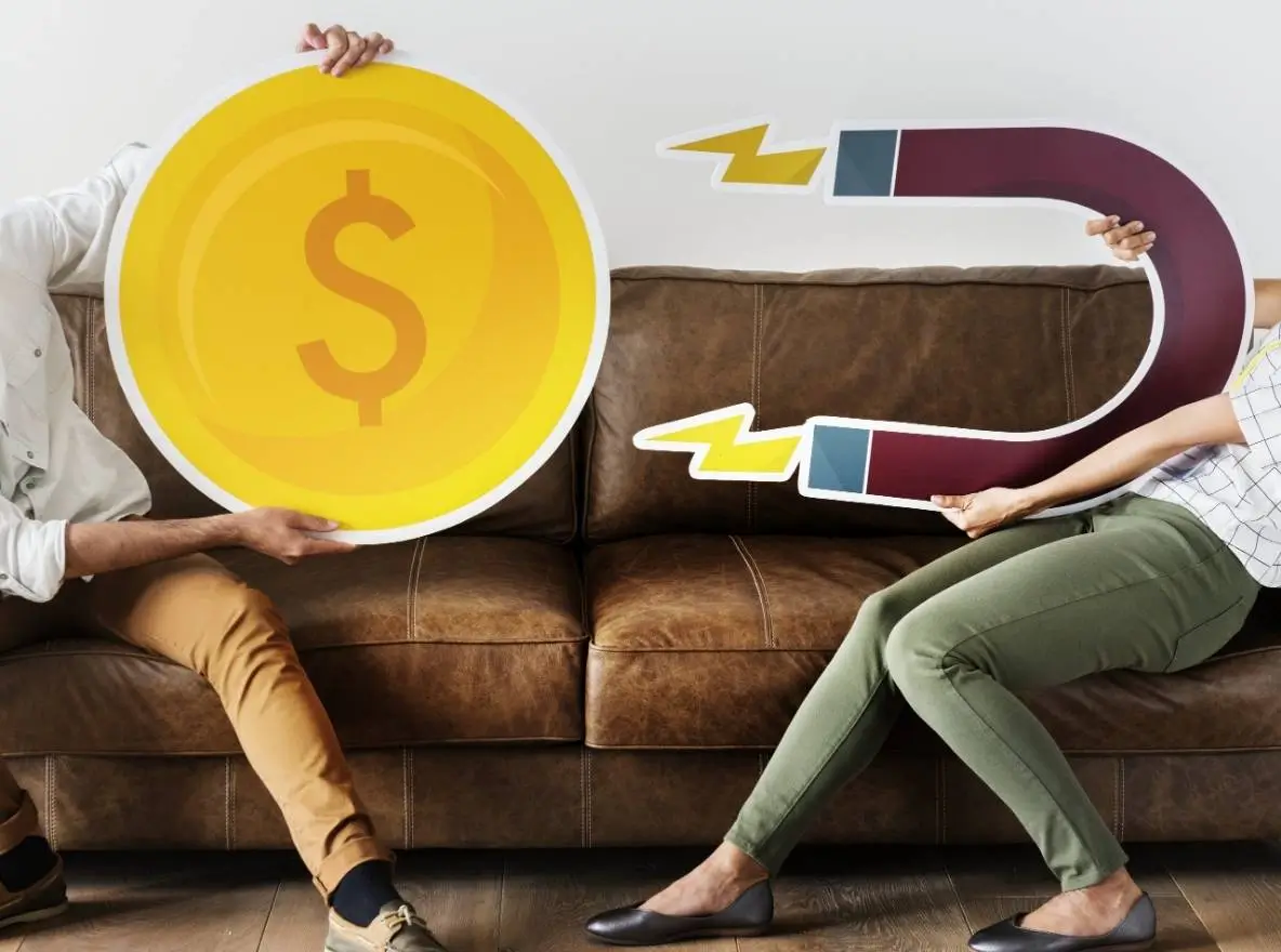 Zwei Personen auf einem Sofa mit großen Magnet- und Münz-Requisiten, die Kundenakquise und Lead-Umwandlung symbolisieren