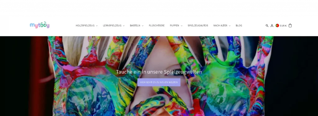 Bunte Nahaufnahme von Kinderhänden, die mit Regenbogenfarben bemalt sind und vor die Gesichter gehalten werden. Im Website-Header sind das MyTooy-Logo und die Spielzeugkategorie-Navigation auf Deutsch zu sehen.
