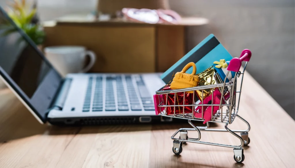 Miniatur-Einkaufswagen mit Produkten vor einem Laptop, der einen Shopify Online-Shop und digitales Einkaufen darstellt