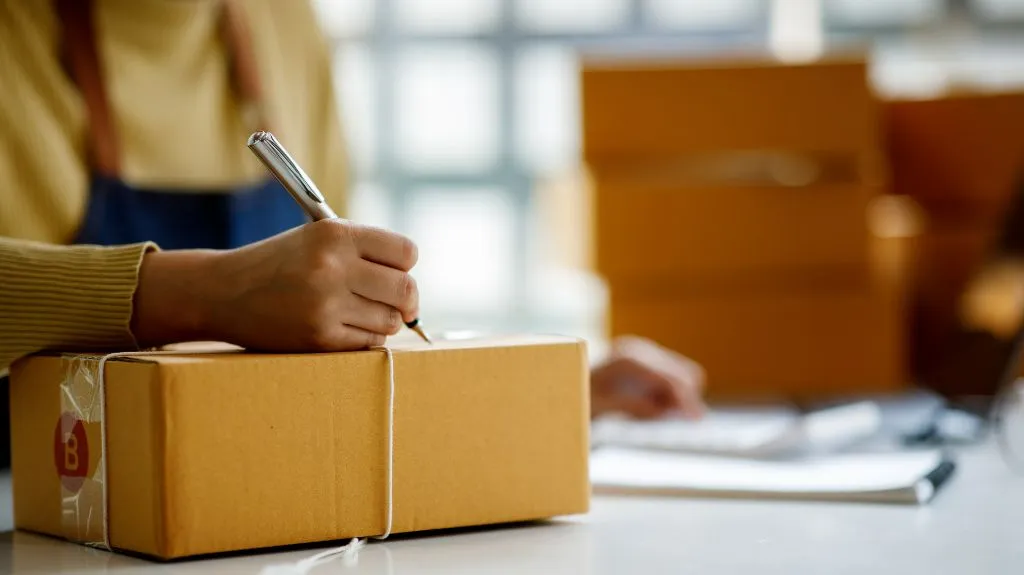 Person beschriftet Paket für Versand durch Dropshipping Lieferanten direkt an den Endkunden